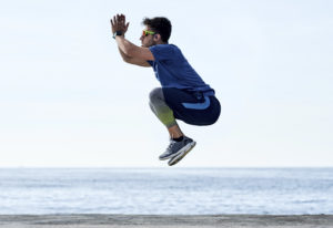 青い空と海を背景に、製品を身に着けジャンプしてトレーニングする男性の写真